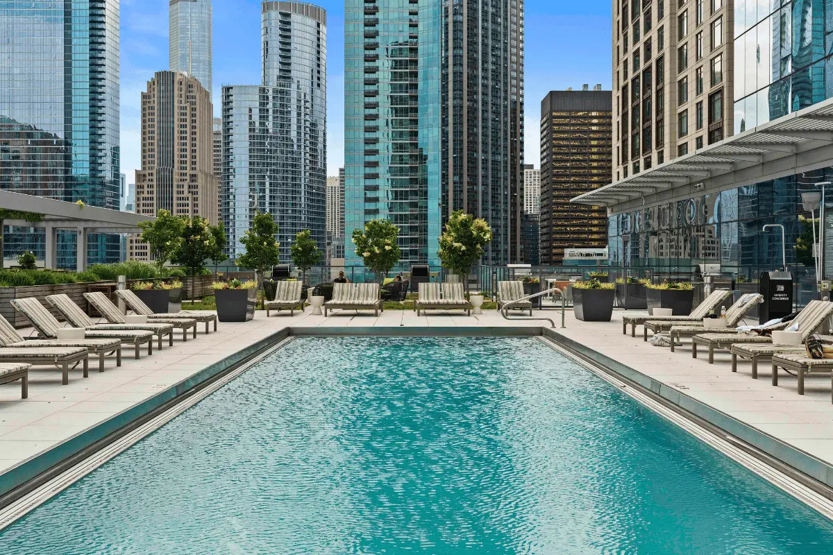 500 Lake Shore Drive's apartment swimming pool with lounge chairs and greenery, surrounded by high-rise buildings in downtown Chicago. The pool area features a modern design with a clear blue sky in the background.