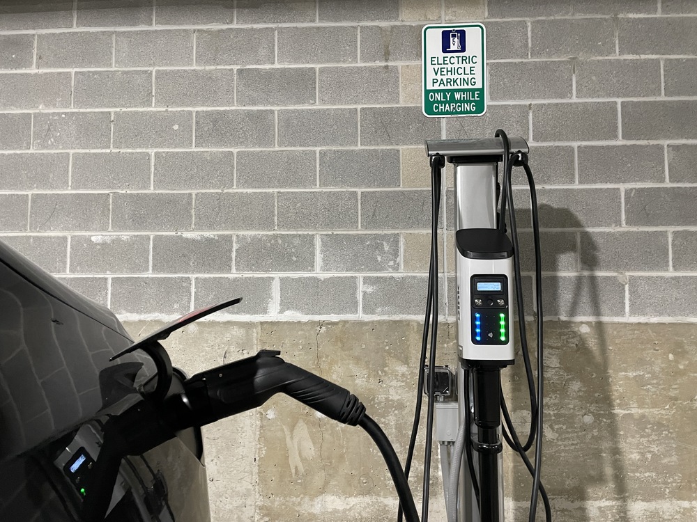 Electric vehicle charging at a station in a parking garage, with a sign above indicating the space is reserved for charging only.